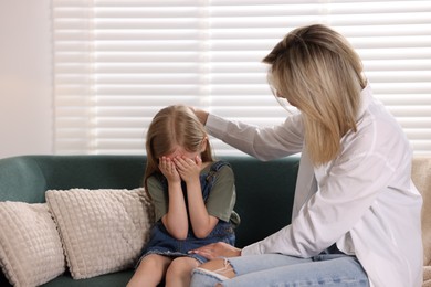 Photo of Mother apologizing to her crying daughter on sofa at home