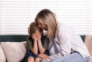 Photo of Mother apologizing to her crying daughter on sofa at home