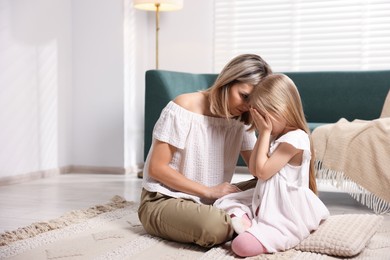 Photo of Mother apologizing to her crying daughter on floor at home. Space for text