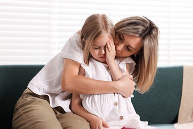 Photo of Mother apologizing to her crying daughter on sofa at home