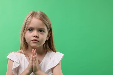 Photo of Little girl with clasped hands apologizing on green background. Space for text