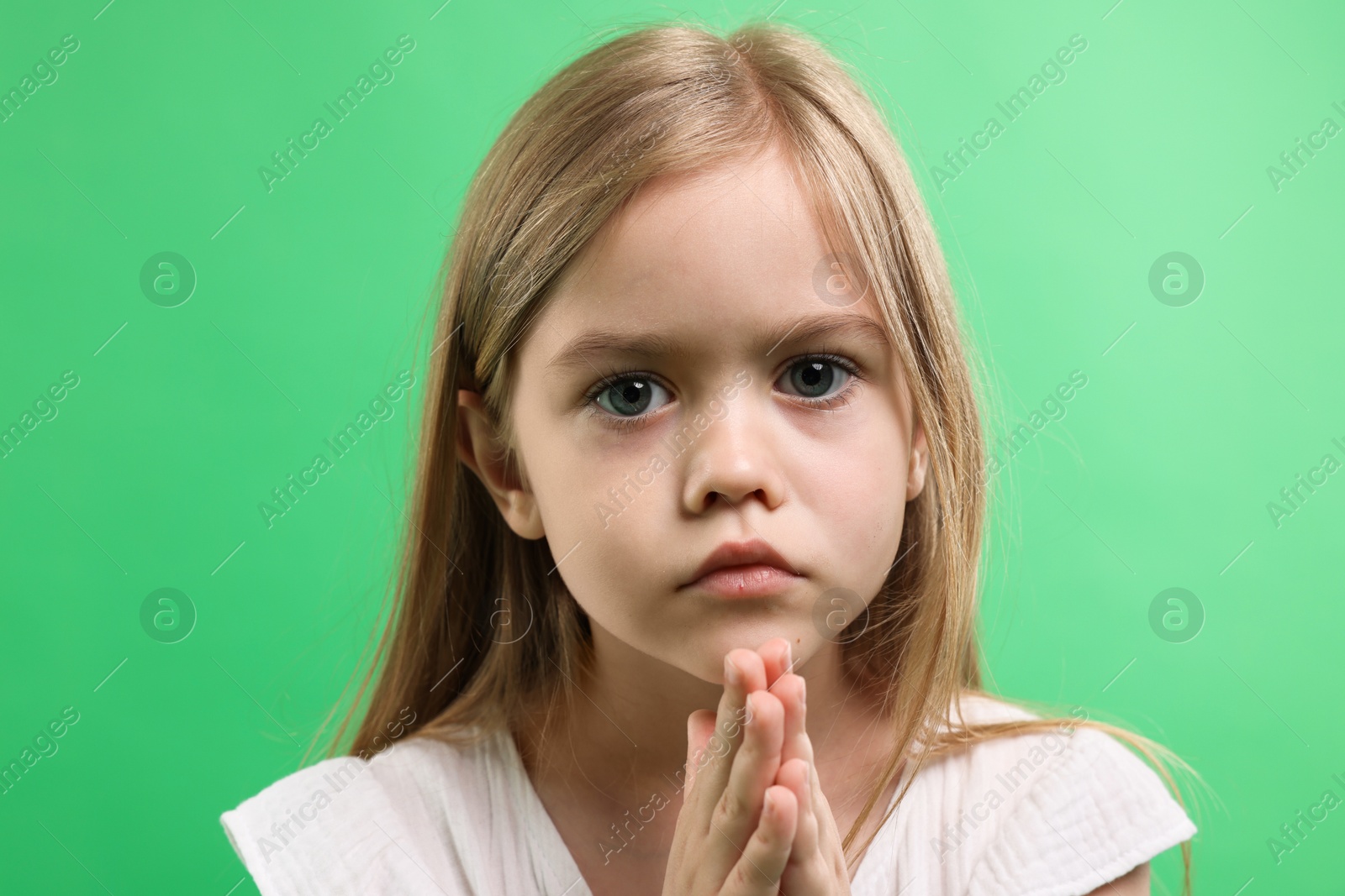 Little girl with clasped hands apologizing on green background, closeup Photo of Little girl with clasped hands apologizing on green background, closeup