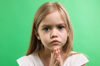 Photo of Little girl with clasped hands apologizing on green background, closeup