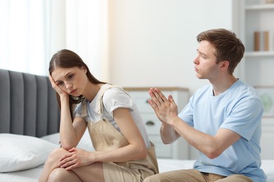 Photo of Man apologizing to his offended girlfriend on bed at home
