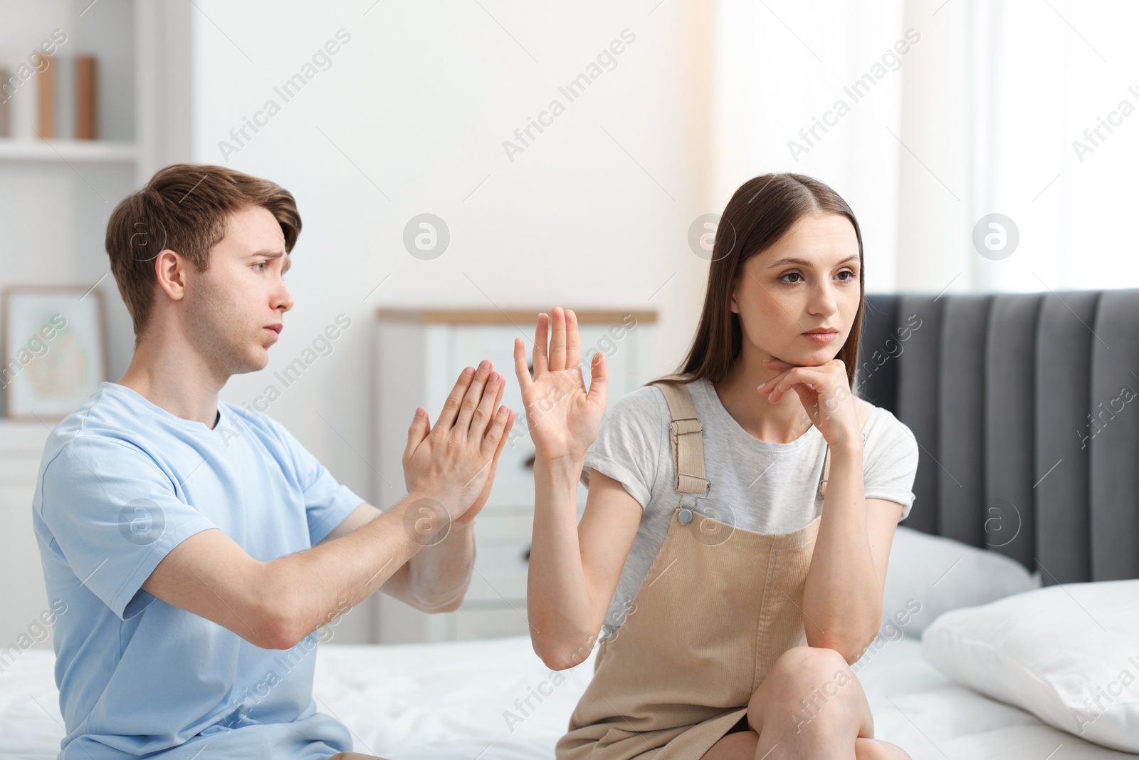 Photo of Man apologizing to his offended girlfriend while she stopping him on bed at home