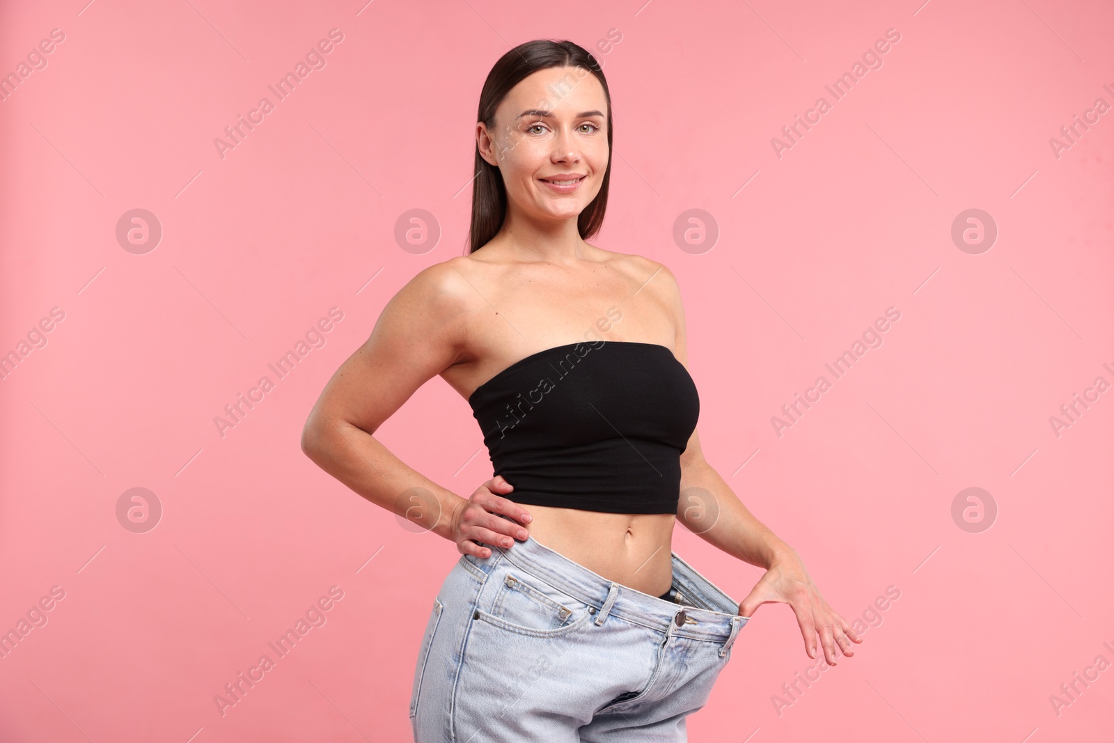 Photo of Fit woman wearing old jeans after weight loss on pink background