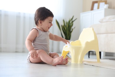 Photo of Cute little baby with potty on floor at home