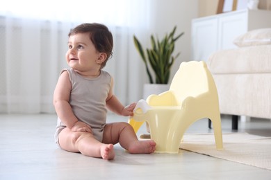 Photo of Cute little baby with potty on floor at home
