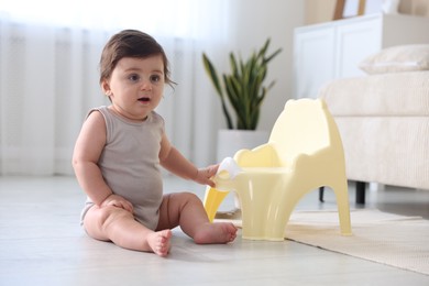 Photo of Cute little baby with potty on floor at home