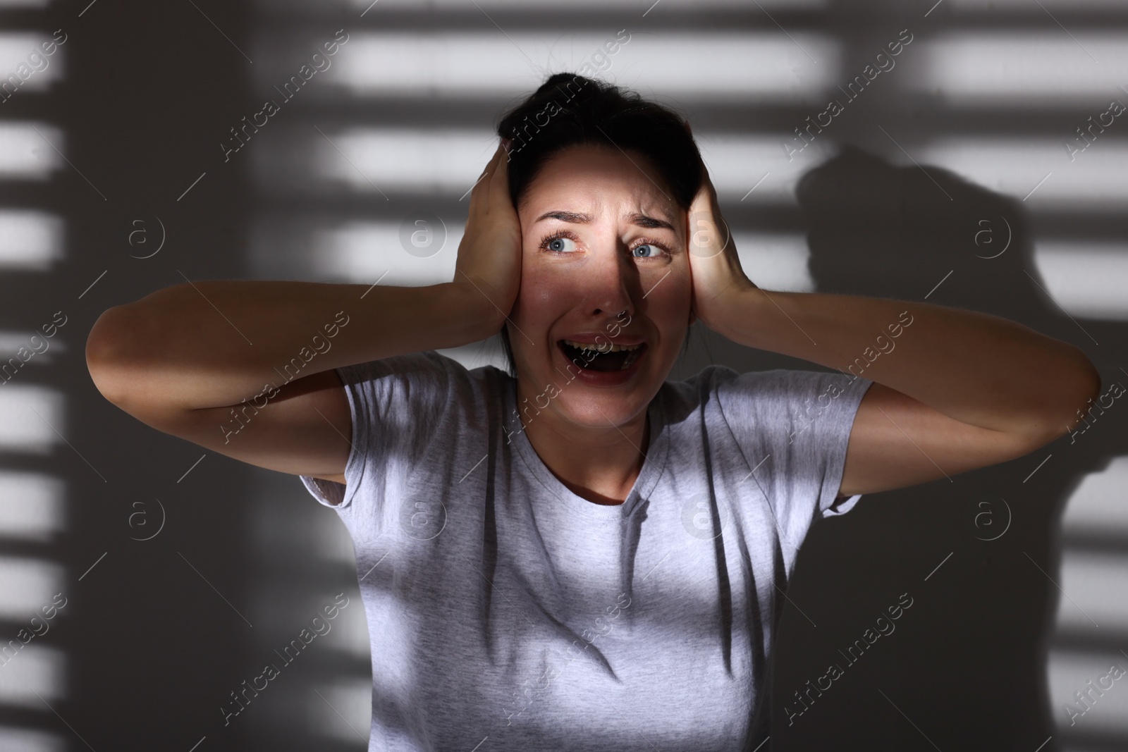 Photo of Emotional woman suffering from panic attack near wall indoors