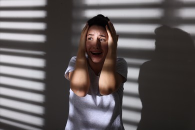 Photo of Emotional woman suffering from panic attack near wall indoors