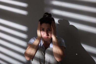 Photo of Emotional woman suffering from panic attack near wall indoors