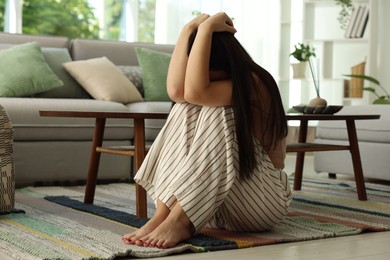Photo of Emotional woman suffering from panic on floor indoors
