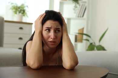 Photo of Emotional woman suffering from panic at table indoors