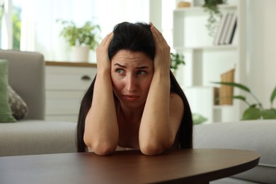 Photo of Emotional woman suffering from panic at table indoors