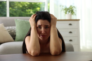 Photo of Emotional woman suffering from panic at table indoors