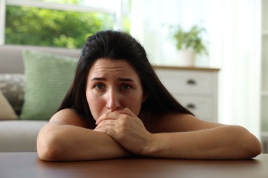 Photo of Emotional woman suffering from panic at table indoors