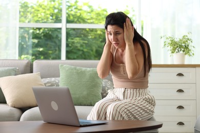Photo of Emotional woman suffering from panic near laptop indoors