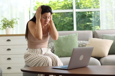 Photo of Emotional woman suffering from panic near laptop indoors