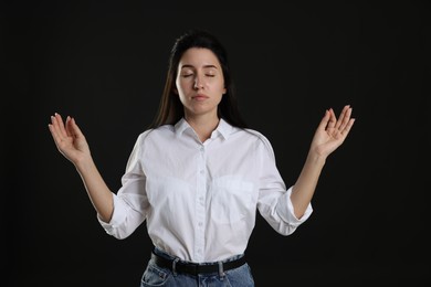 Photo of Panic attack. Woman meditating to calm down on black background