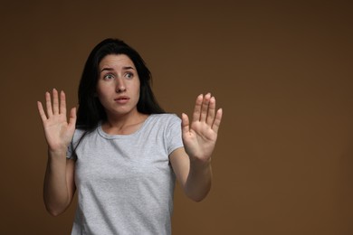 Photo of Worried woman suffering from panic attack on brown background, space for text