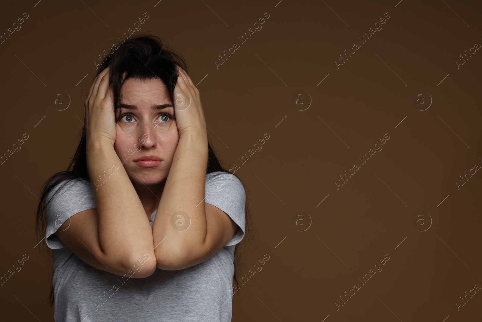 Photo of Worried woman suffering from panic attack on brown background, space for text