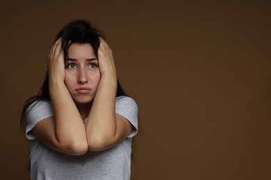 Photo of Worried woman suffering from panic attack on brown background, space for text