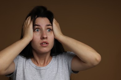 Photo of Worried woman suffering from panic attack on brown background
