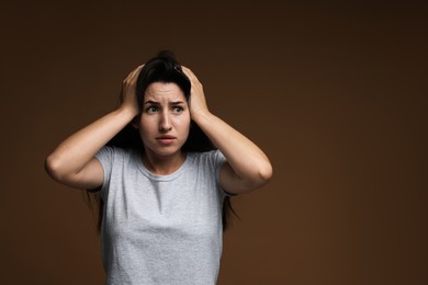 Photo of Worried woman suffering from panic attack on brown background, space for text