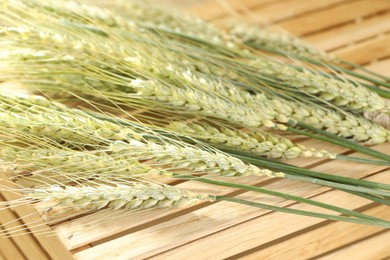 Photo of Green wheat spikes on wooden crate, closeup