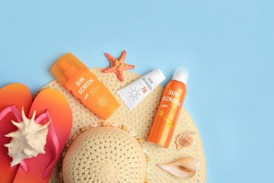 Image of Sunscreens, flip flops and hat on light blue background, top view. Sun protection product