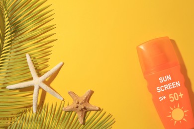 Image of Sunscreen in bottle, sea stars and green palm leaves on orange background, top view. Sun protection product
