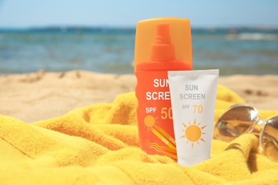 Image of Sunscreens, sunglasses and towel on beach. Sun protection product