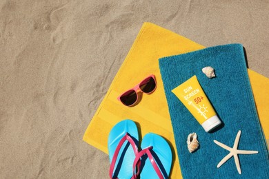 Image of Sunscreens, flip flops, sunglasses and towels on sand, top view. Sun protection product