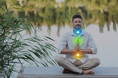Image of Man meditating in Lotus pose on pier near river. Glowing bubbles representing chakras