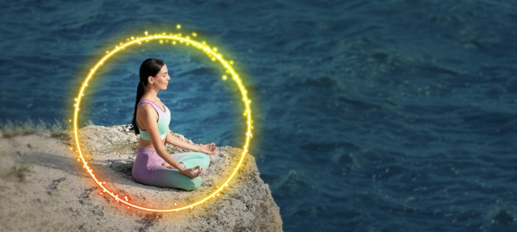 Image of Woman meditating in Lotus pose on cliff near sea. Bright bubble around her representing aura