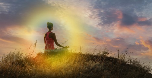 Image of Woman meditating in Lotus pose in nature. Glowing bubble around her representing aura