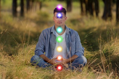 Image of Man meditating in Lotus pose in nature. Rainbow lights representing chakras