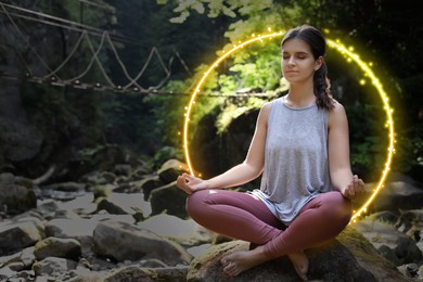 Image of Woman meditating in Lotus pose in mountains. Bright bubble around her representing aura