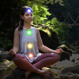 Image of Woman meditating in Lotus pose in mountains. Rainbow lights representing chakras