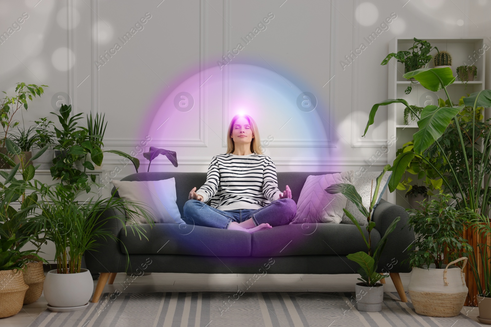 Image of Woman meditating in Lotus pose at home. Bright bubble around her representing aura