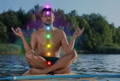 Image of Man meditating in Lotus pose on SUP board. Rainbow lights representing chakras. Aura around him