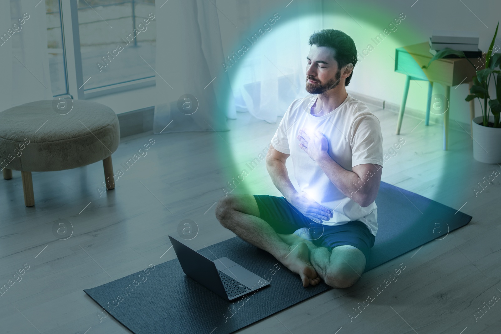 Image of Man meditating in Lotus pose at home. Rainbow bubble around him representing aura