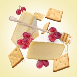 Image of Cheese, grapes, crackers and honey in air on beige gradient background. Tasty appetizers for cheese board