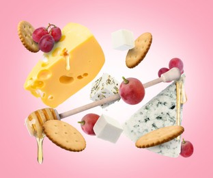 Image of Cheese board products in air on pink gradient background. Different types of cheese, grapes, crackers and honey