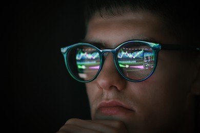 Photo of Young man wearing glasses with reflection on black background, closeup