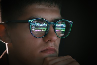 Photo of Young man wearing glasses with reflection on black background, closeup