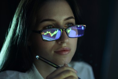 Photo of Young woman wearing glasses with reflection on dark background, closeup