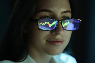 Photo of Young woman wearing glasses with reflection on dark background, closeup