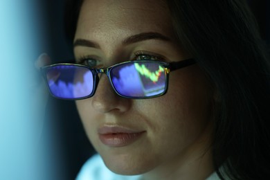 Photo of Young woman wearing glasses with reflection on dark background, closeup
